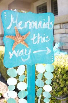 a blue sign that says mermaids this way with a starfish hanging from it