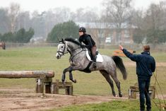 a person riding on the back of a horse jumping over a wooden obstacle in an open field