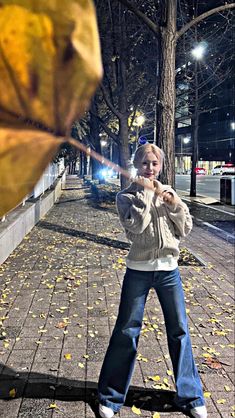 a young boy swinging a baseball bat on a sidewalk at night time with leaves all over the ground