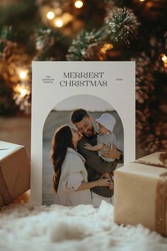 a christmas card with a photo of a man and woman holding a baby in front of a tree