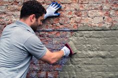 a man in grey shirt and white gloves painting a brick wall