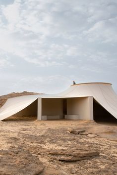 a white tent sitting on top of a dirt field next to a desert area with rocks