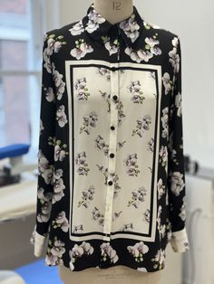 The Shutters Classic Silk Shirt is a button-through Italian silk crepe de chine shirt with a stunning monochrome placement orchid print. The beautiful orchids are painted by Kate Scott, a botanical digital fine artist who has worked with Suzannah for 10 years. Kate paints the flowers with a digital tool at high resolution, with the florals appearing clearer than a photograph, as if they can be plucked from the cloth. Kate's work has been exhibited globally and in the Saatchi gallery. Expertly printed by a premium mill in Italy, the absolute finest techniques were used to translate this incredible art onto the beautiful silk crepe. Featuring full length cuffed sleeves, simple silk covered buttons, and a deep box pleat at the back, the Shutters Shirt has a beautiful elegance and fluidity to Designer Silk Shirt With Floral Print, Silk Shirt With Floral Print And Spread Collar, Elegant Silk Blouse With Digital Print, Designer White Blouse With Floral Print, Designer Floral Print Button-up Blouse, Designer Button-up Blouse With Floral Print, Elegant Graphic Print Workwear Blouse, Silk Top With Floral Print And Spread Collar, Elegant Graphic Print Blouse For Work