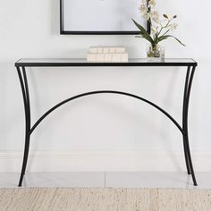 a black console table with flowers and books on it in front of a white wall