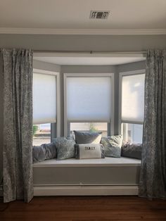 a window seat with pillows on it in the middle of a living room next to two windows