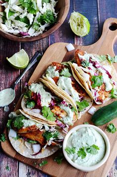 chicken tacos with guacamole sauce and lime wedges on a cutting board