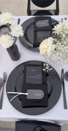 the table is set with black plates and silverware, white flowers in vases