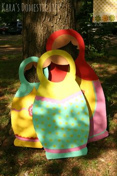 two colorful bags are sitting next to a tree in the grass and one is made out of paper