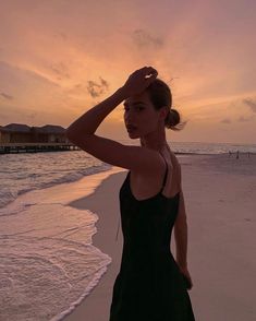 a woman standing on top of a sandy beach next to the ocean at sun set