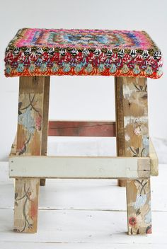 an old wooden stool with a colorful cushion on top