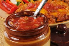 a jar filled with sauce sitting next to a plate of food on top of a table