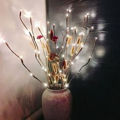 a vase filled with flowers and lights on top of a table next to a wall