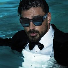 a man in a tuxedo and sunglasses is floating in the water with his hands on his hips