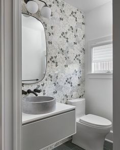 a white toilet sitting next to a sink in a bathroom under a mirror and light fixture