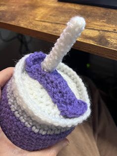 a hand holding a crocheted purple and white cup with a straw sticking out of it