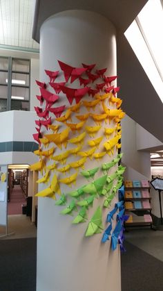 many colorful origami birds are hanging on the side of a wall in an office building