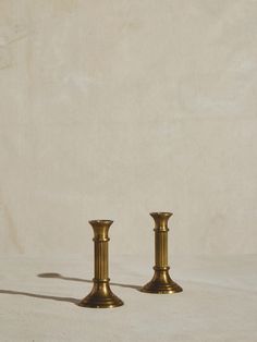 two brass candlesticks sitting side by side on a white surface with a shadow from the candle