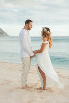 a man and woman standing on top of a sandy beach next to the ocean holding hands