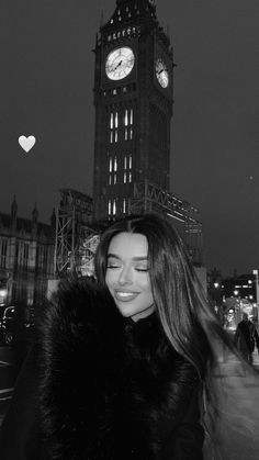 a woman standing in front of a clock tower at night with her hair blowing in the wind