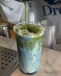 a person pours green tea into a tall glass with ice on the rim and sprinkles