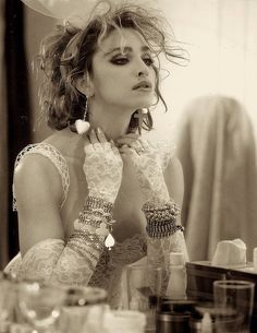 a woman with her hands on her face sitting in front of a mirror wearing gloves and bracelets