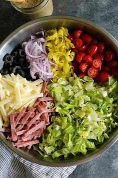 a bowl filled with lettuce, tomatoes, olives and other ingredients next to a jar of mustard