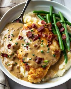 a white bowl filled with mashed potatoes covered in gravy and green beans