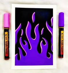 two pens are sitting next to an art print with purple and black flames on it