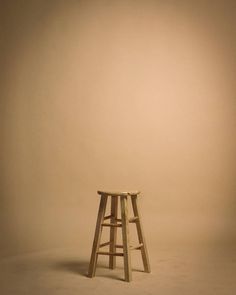 a wooden stool sitting on top of a white floor next to a light brown wall