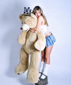 a young woman hugging a giant teddy bear wearing a tiara and holding it in her arms