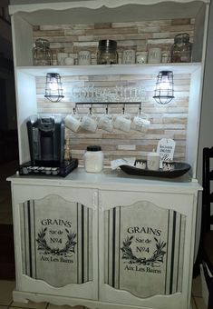 a white cabinet with two doors and some cups on it's shelf next to a coffee maker