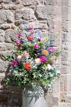 a vase filled with lots of colorful flowers on top of a stone floor next to a brick wall