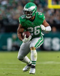 a football player running with the ball in his hand and wearing a green uniform on