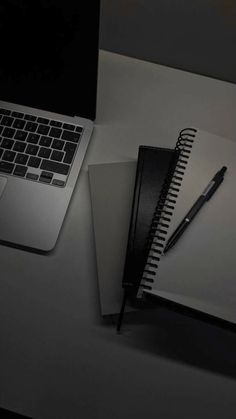 an open notebook sitting on top of a desk next to a laptop computer and a pen