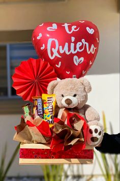 a teddy bear sitting on top of a box filled with candy and a heart shaped balloon