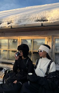 two women sitting on the ground in front of a building with snow covered roof and windows