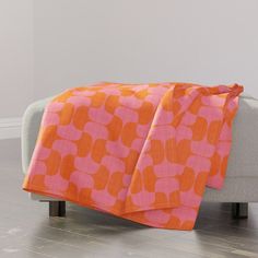 an orange and pink blanket sitting on top of a couch next to a white chair