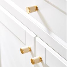 two brass knobs are on the handles of a white cabinet with gold trimming