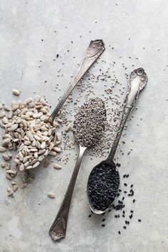 two spoons filled with seeds next to each other on top of a cement surface