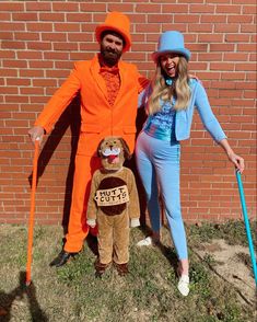 a man and woman in costumes standing next to each other near a brick wall with an orange costume on