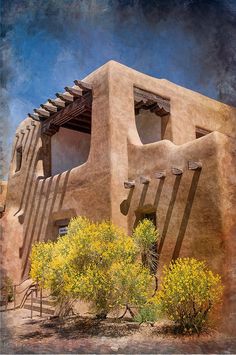 an adobe building with trees and bushes in front