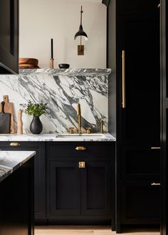 a kitchen with black cabinets and marble counter tops, gold handles and brass pulls on the faucets