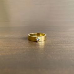 a gold ring with a single diamond on the side sitting on a wooden table top