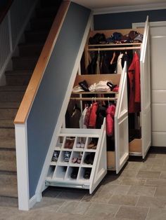 an open closet under stairs with shoes and coats