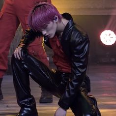 a man with pink hair and black pants crouching on the ground in front of other men