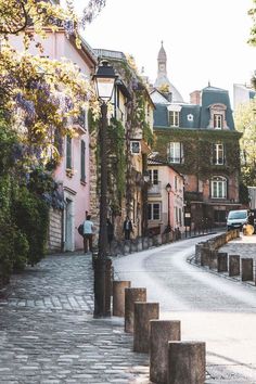 a cobblestone street lined with tall buildings and trees in front of the sidewalk