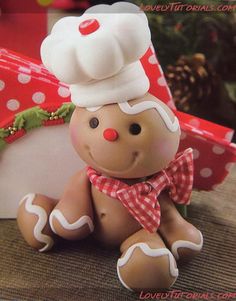 a teddy bear wearing a chef's hat sitting next to a gift box and christmas tree