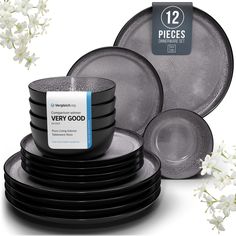 a stack of black and grey plates with white flowers in the background, including one that says very good