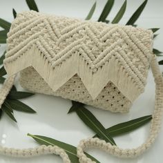 a white purse sitting on top of a table next to some green leafy plants