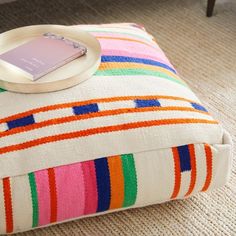 a white plate sitting on top of a multi colored ottoman cushion next to a coffee table